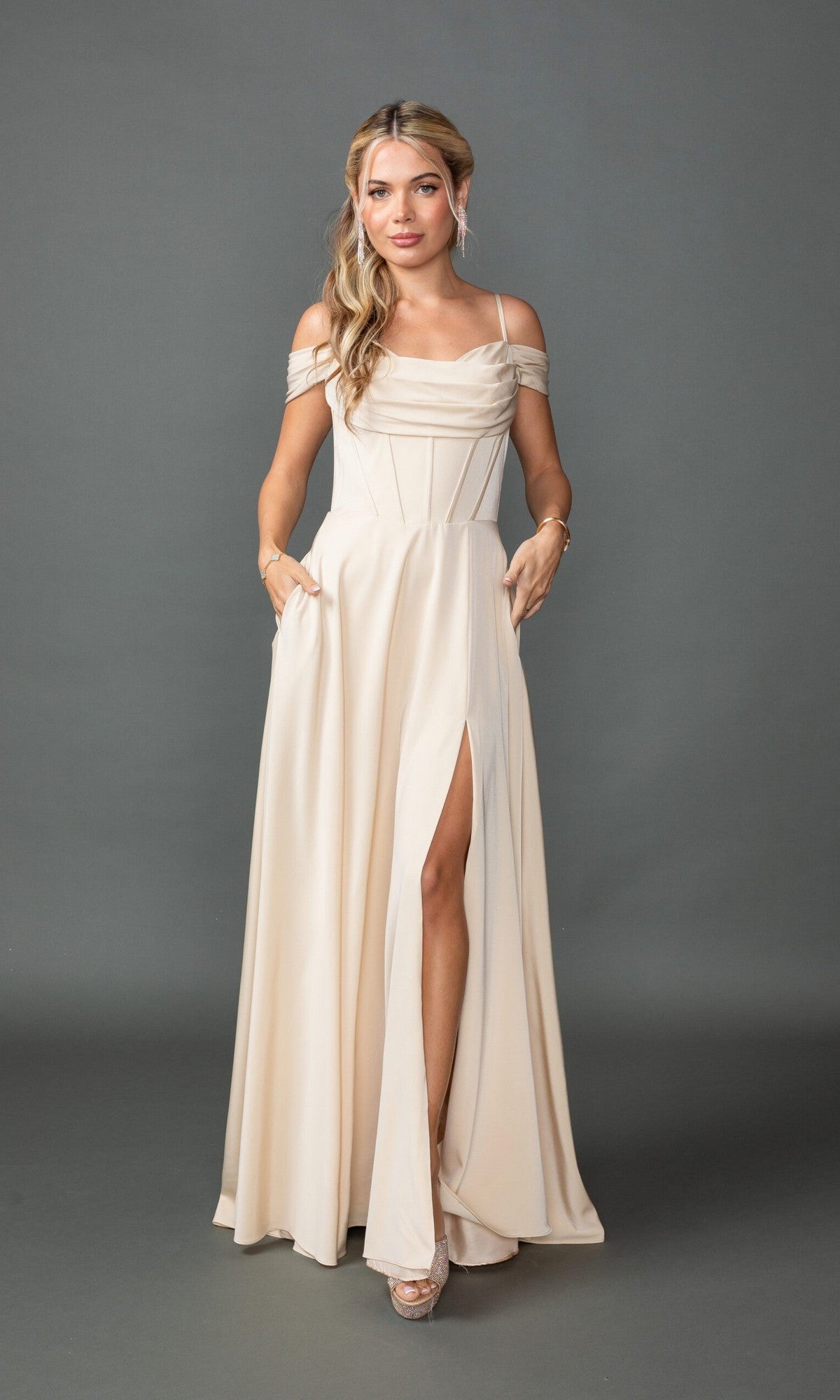 Model showcasing the Dancing Queen 4539, a long ivory A-line prom dress with an off-shoulder neckline and thigh-high leg slit, posing against a plain gray background.